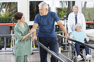 A rehab therapist with a resident needing assistance walking while holding handrails